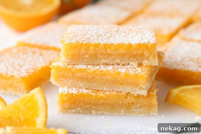 Golden Citrus Bars 9 A close-up of a perfectly stacked trio of orange bars, glistening with powdered sugar, inviting a bite.