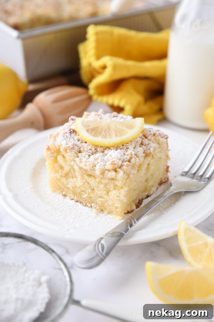 Zesty Lemon Coffee Cake 2 A thick slice of vibrant Lemon Coffee Cake, dusted with powdered sugar and garnished with a fresh lemon slice, presented on a white plate.