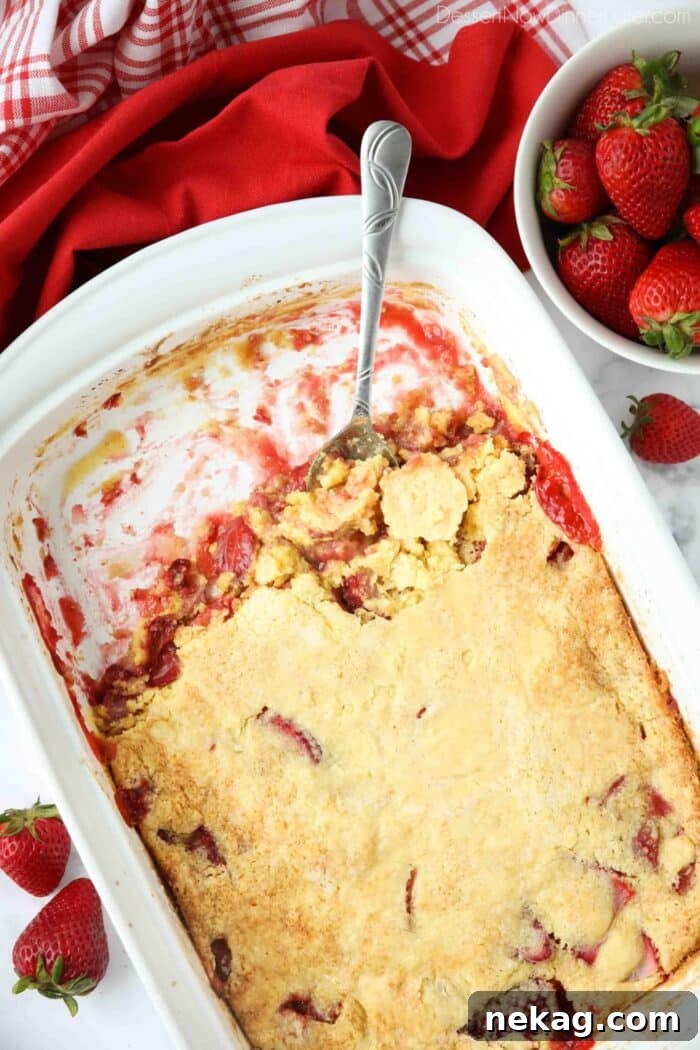Effortless Strawberry Delight 3 A pan of freshly baked Strawberry Dump Cake with a spoon scooping out a portion, showcasing the juicy strawberry base and golden cake topping.