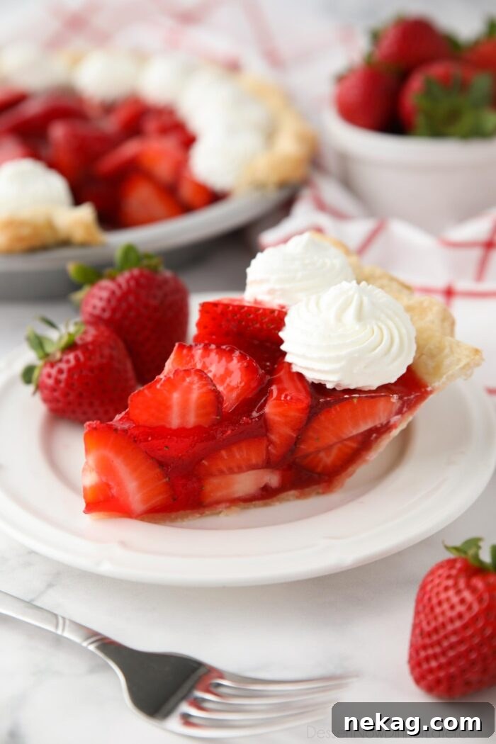 Slice of fresh strawberry pie on a plate with whipped cream piped on top.