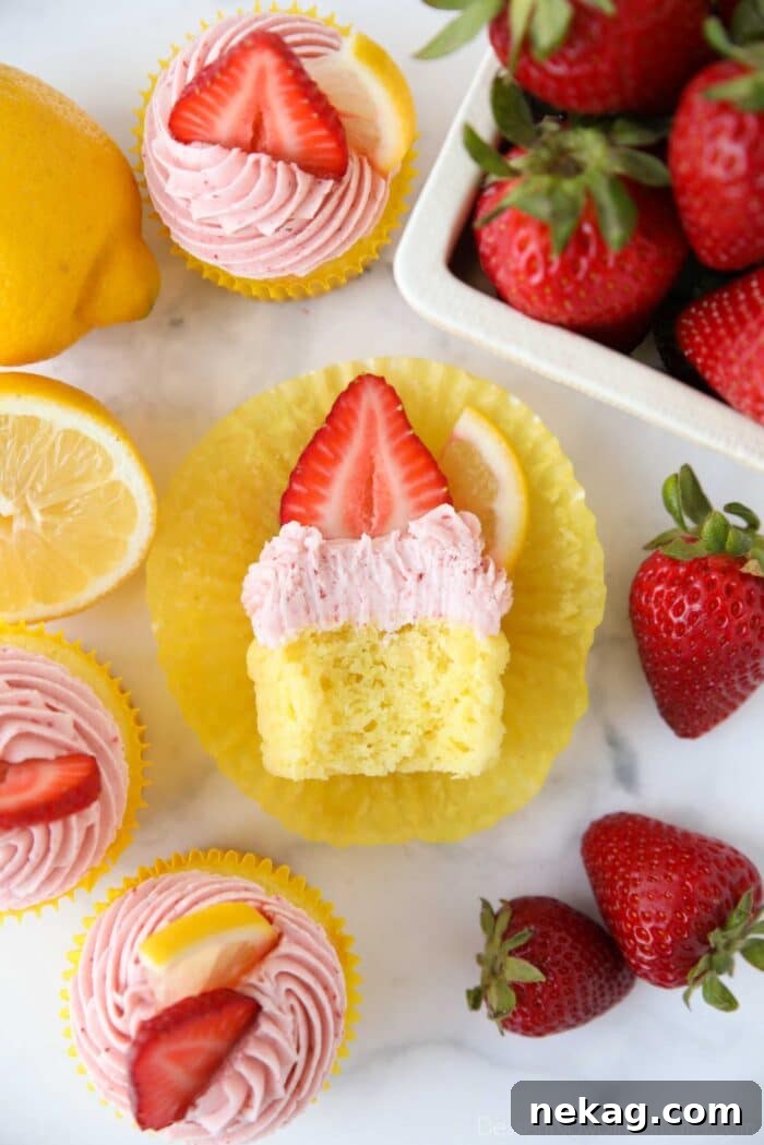 Sunshine Strawberry Lemonade Cupcakes 4 Strawberry lemonade cupcake with a bite taken out showing the inside of a fluffy lemon cupcake with strawberry frosting.