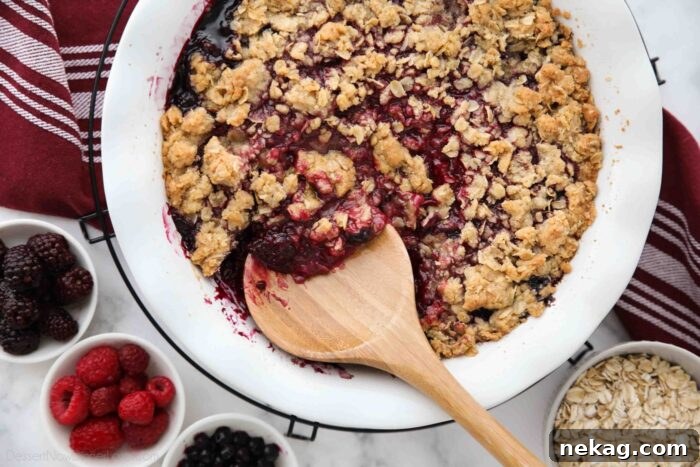 A close-up of warm, baked berry crisp being spooned out of a deep pie dish, ready to be served.