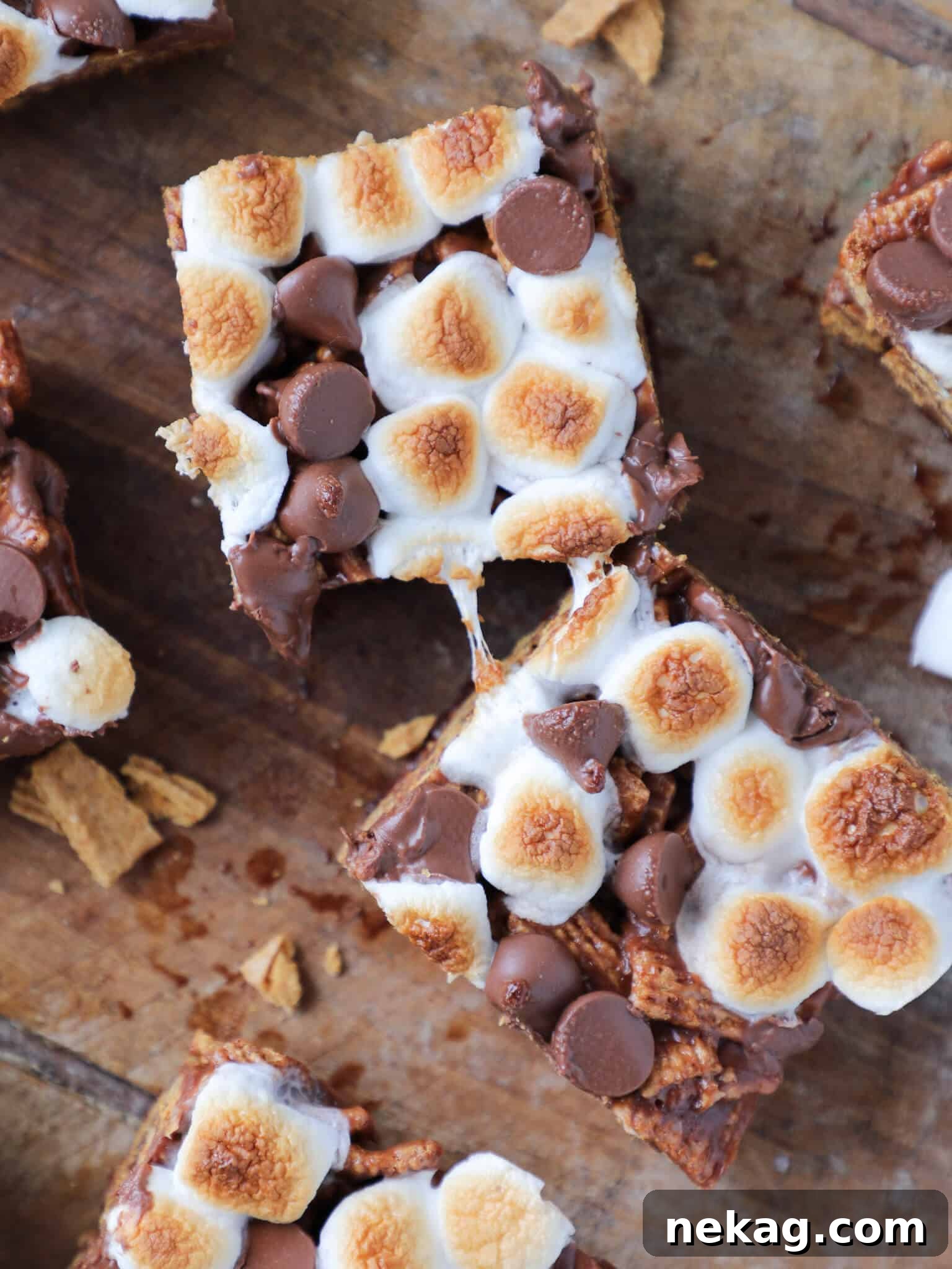 A hand pulling apart a sliced No Bake Golden Graham S'mores Bar, demonstrating the stretchy, gooey toasted marshmallow texture on a wooden surface.