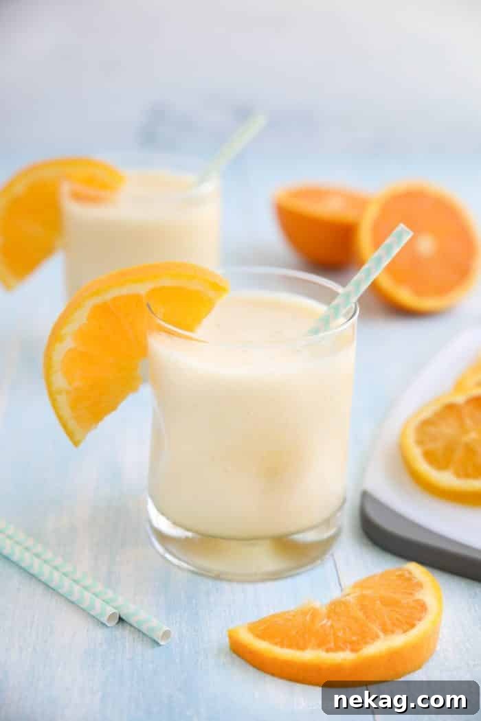 Perfect Homemade Orange Julius 2 Orange Julius smoothie in a cup with a straw and fresh orange slices.