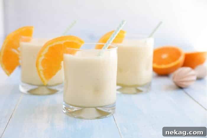 Perfect Homemade Orange Julius 3 Orange Julius smoothies in cups with straws and fresh orange slices.