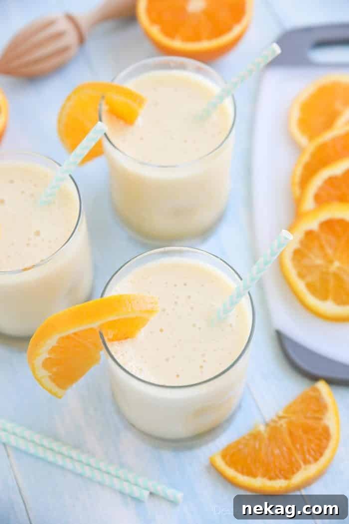 Perfect Homemade Orange Julius 4 Orange Julius smoothies in cups with straws and fresh orange slices.