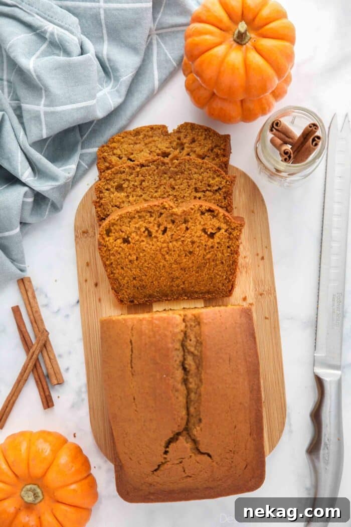 A whole pumpkin loaf cake on a wooden cutting board with several slices already cut off, ready to be enjoyed.