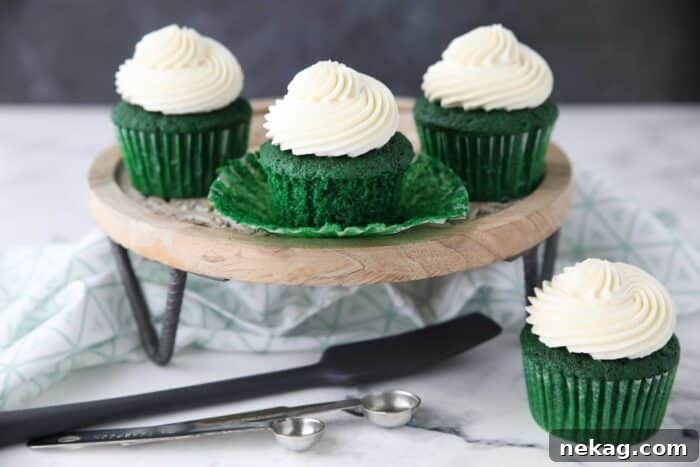 Jade Velvet Cupcakes 11 Green velvet cupcakes on a cake stand, one with its paper wrapper peeled down to show the vibrant green cake inside.