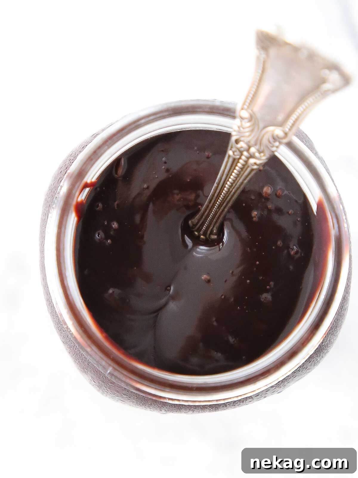 A rustic glass jar filled with thick, glossy homemade chocolate fudge sauce.