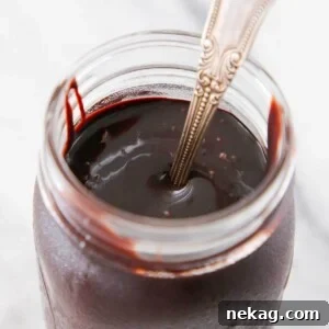 Thick, glossy chocolate fudge sauce in a glass jar, ready to be served.