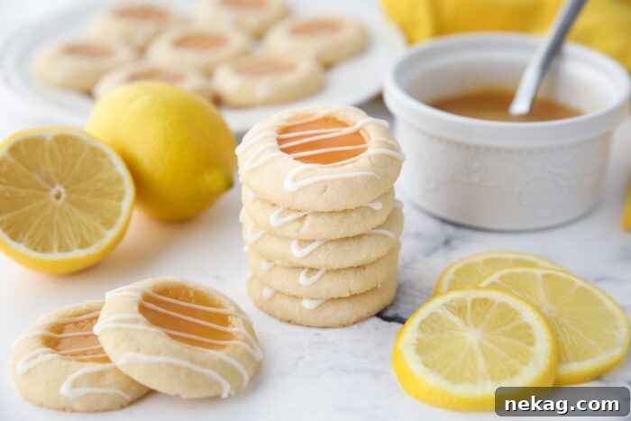 Tangy Lemon Delights 11 A tantalizing close-up of a stack of golden lemon thumbprint cookies, beautifully accented with a fine drizzle of white lemon glaze. The glistening lemon curd filling is visible in the center, promising a burst of fresh, tangy flavor within the tender shortbread.