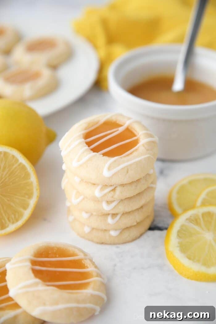 Tangy Lemon Delights 3 A beautiful stack of three golden lemon thumbprint cookies, each showcasing a glistening lemon curd center and delicately drizzled with white lemon glaze. The soft, buttery texture of the shortbread is evident, inviting a taste of their tangy-sweet goodness.