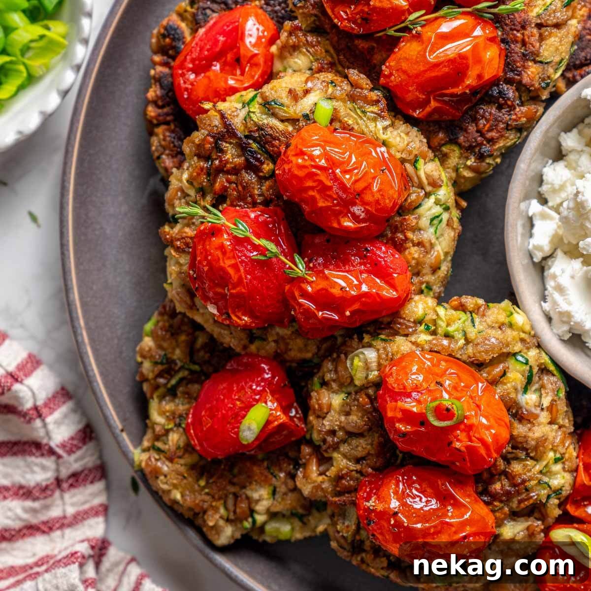 Four golden zucchini fritters elegantly plated with slow-roasted tomatoes and crumbled goat cheese, ready to be served.