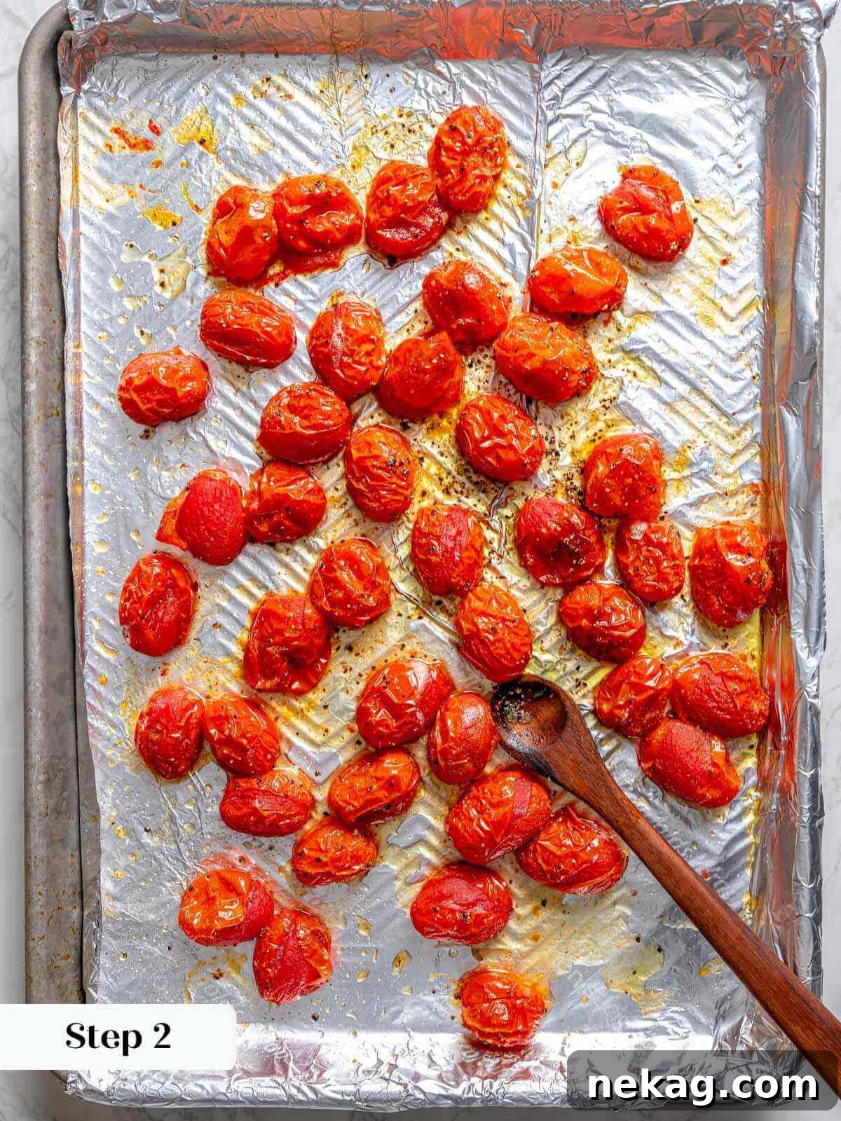 Slow-roasted tomatoes spread in a single layer on a foil-lined baking sheet, their juices slightly caramelized.