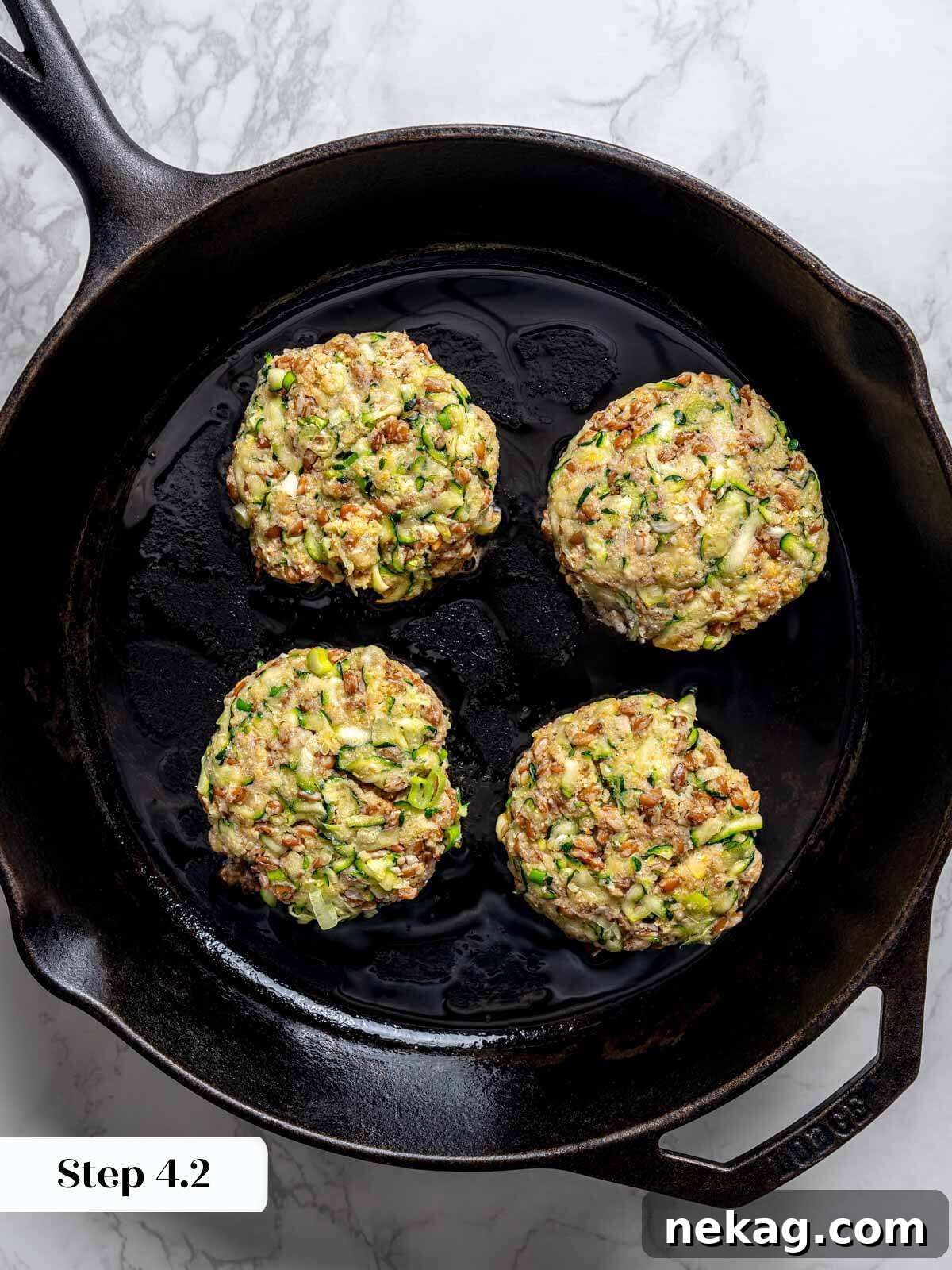 Four perfectly shaped, uncooked zucchini fritter patties nestled in a cast iron pan, ready for frying.