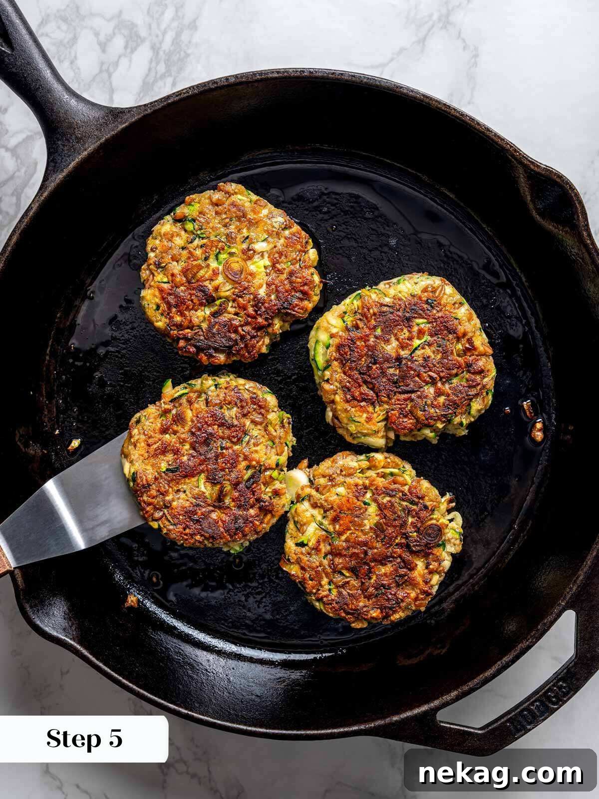 Four perfectly cooked zucchini fritter patties, golden brown and crispy, resting in a cast iron pan.