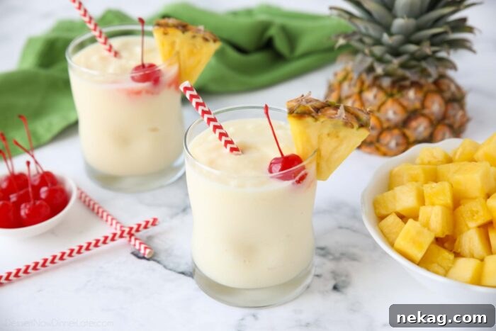 Virgin pina coladas in glass cups with a wedge of pineapple, a maraschino cherry, and a straw.