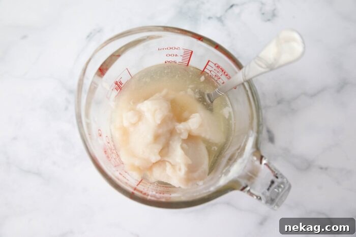 Separated Cream of Coconut from a can inside a glass measuring cup with a fork to stir it up.