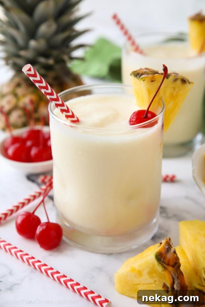 Non alcoholic pina colada mocktail in a glass cup with a wedge of pineapple, a maraschino cherry, and a straw.