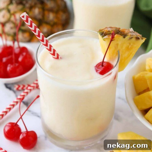 Virgin pina colada in a glass cup with a wedge of pineapple, a maraschino cherry, and a straw.