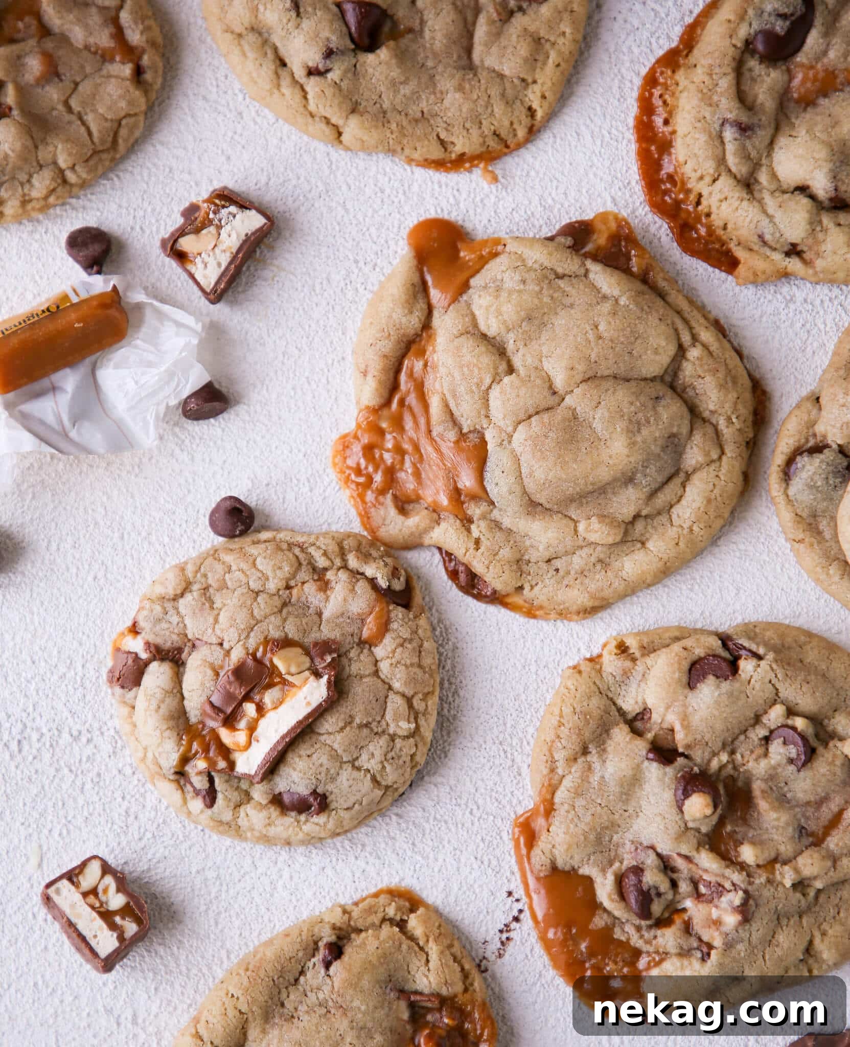 Brown Butter Snickers Caramel Core Chocolate Chip Cookies 2 Delicious Caramel Stuffed Brown Butter Snickers Chocolate Chip Cookies arranged on a white surface, showcasing their golden-brown edges and gooey centers.