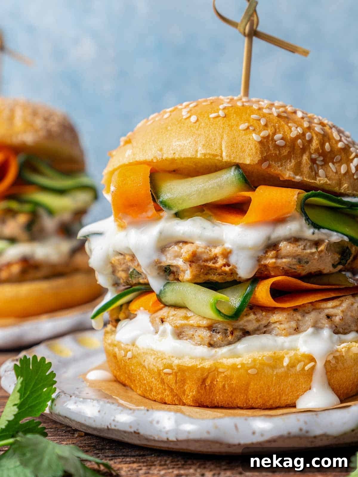 Ultimate Chicken Burgers 2 chicken burger stacked with fresh vegetables and a generous dollop of sauce on a bun.