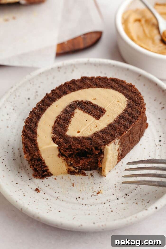 Velvet Chocolate Roulade 7 Bite taken out of a slice of chocolate roll cake with whipped peanut butter filling on a plate.