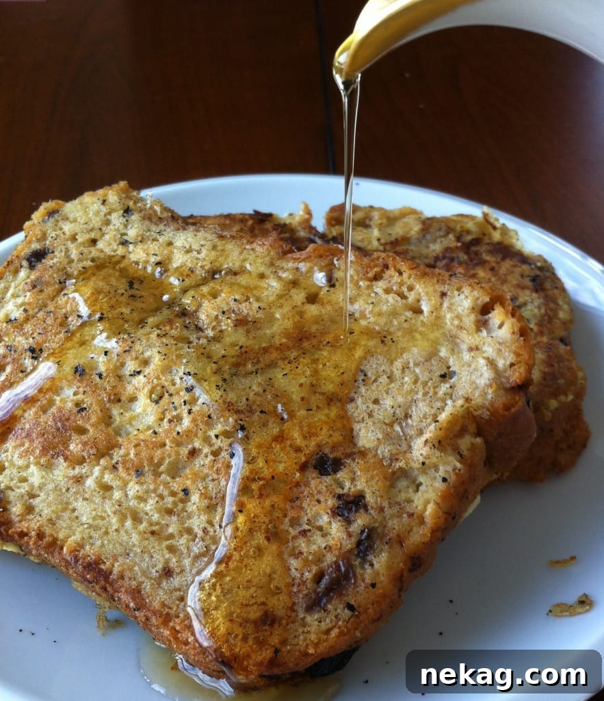 Golden brown Cinnamon Raisin French Toast with warm maple syrup drizzled over it, garnished with a sprinkle of powdered sugar.
