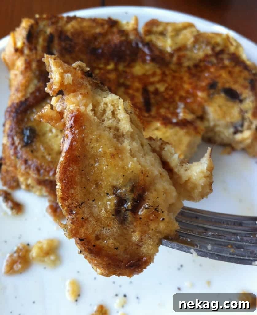 A close-up of Cinnamon Raisin French Toast with a bite taken out, showing its fluffy interior and visible raisins.