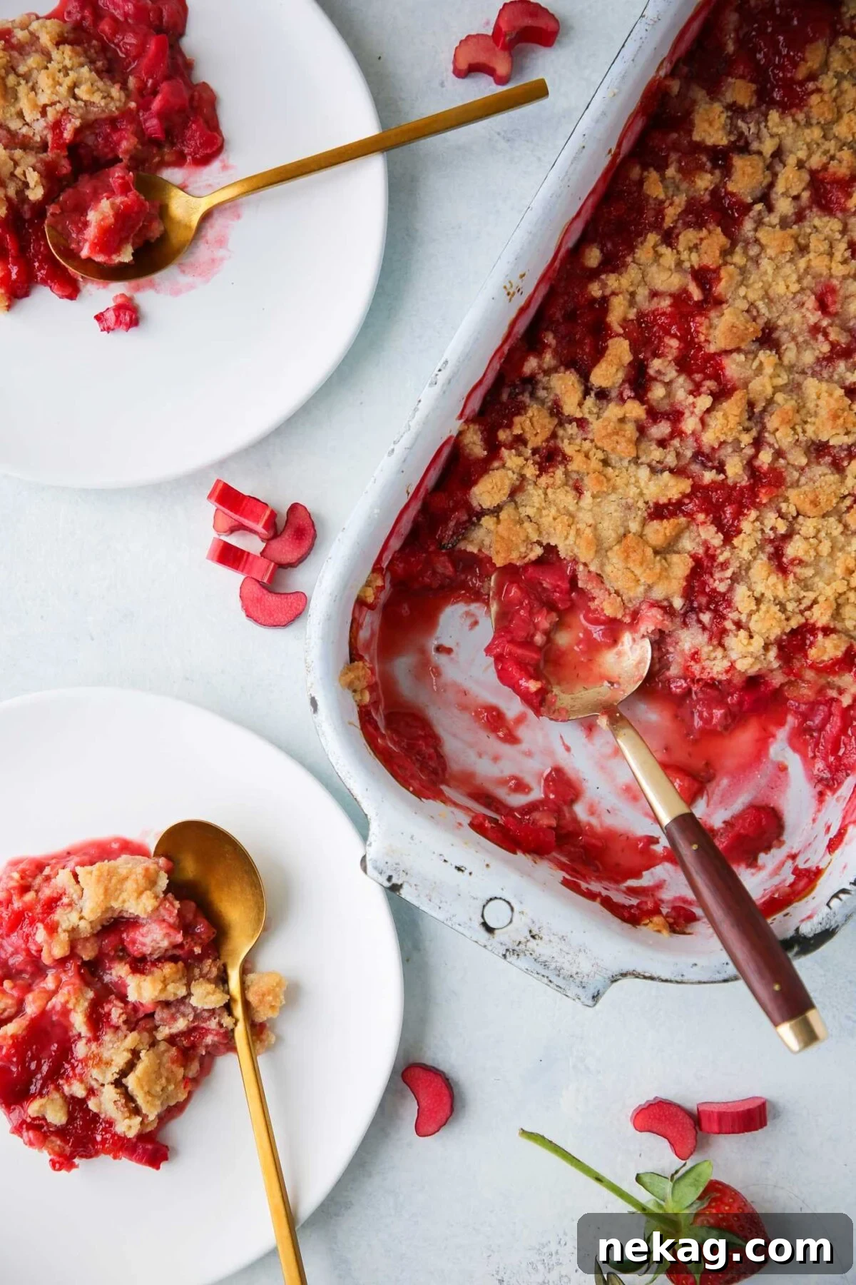 Individual servings of strawberry rhubarb crumble on white plates with elegant gold spoons, inviting a taste.
