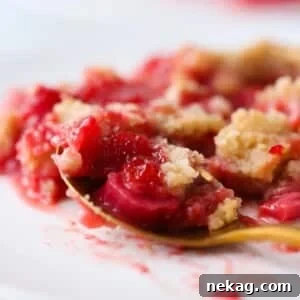 Close-up of juicy strawberries and rhubarb baked under a golden crumble topping, a delightful summer treat.