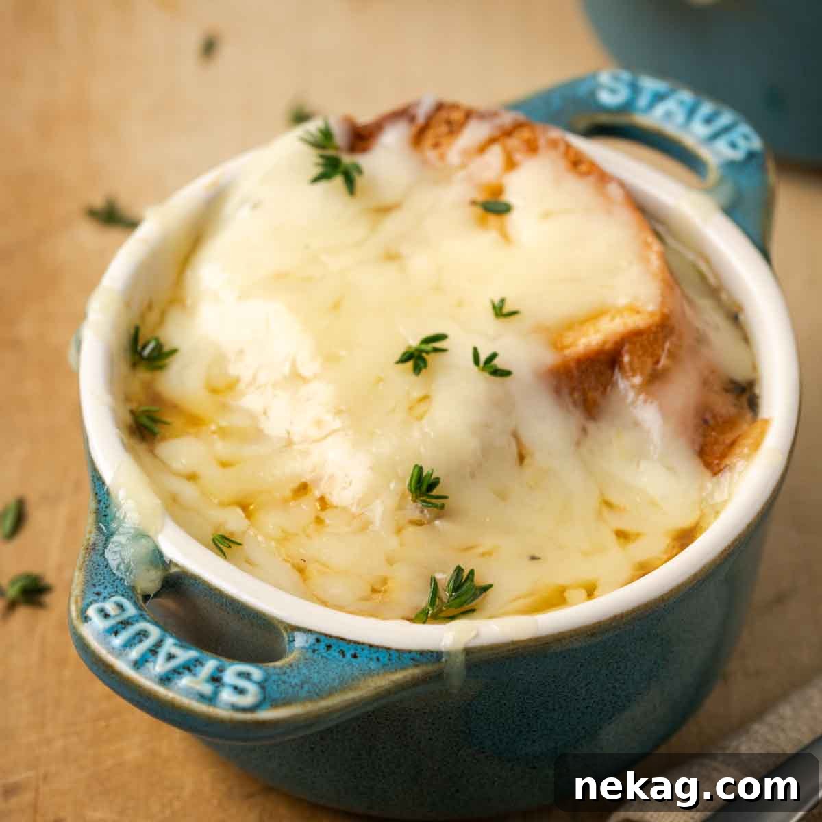 Quintessential French Onion Soup 3 melted cheese on top of small staub baking dish, showing a perfect golden-brown crust.