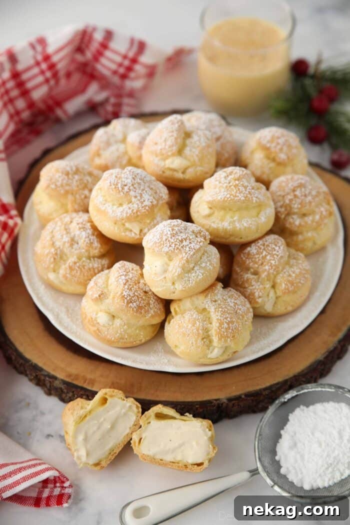 Holiday Eggnog Cream Puffs 4 Close-up of three eggnog cream puffs on a white plate, one sliced open to reveal the fluffy eggnog cream filling.