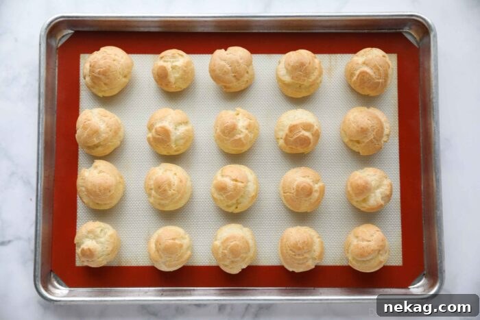 Holiday Eggnog Cream Puffs 7 Freshly baked golden brown cream puffs resting on a sheet tray after being removed from the oven.