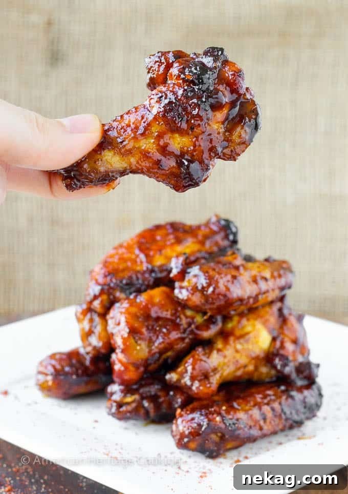 Sweet Heat Crispy Baked Wings 2 A stack of perfectly baked chicken wings with one wing being held up, showcasing its crispy skin and saucy glaze.