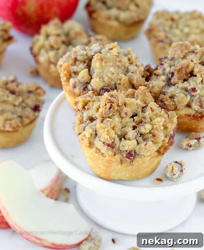 Handheld Apple Delights 3 mini apple pies with pecan crumble on top on small white cake stand.