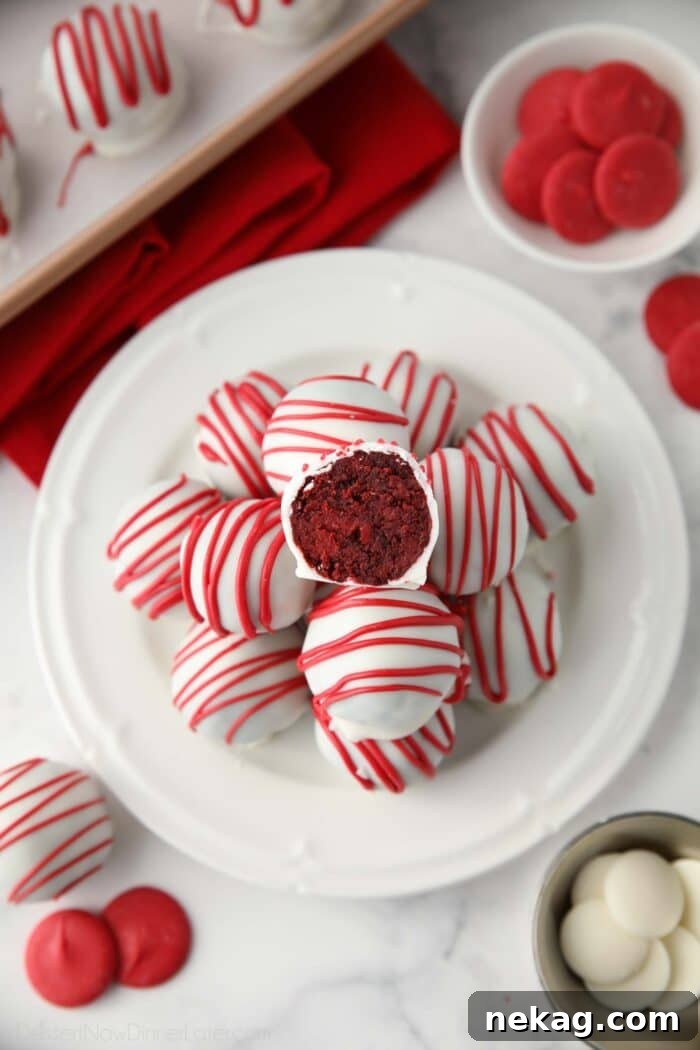 Decadent Red Velvet Bites 3 A stunning arrangement of Red Velvet Cake Truffles on a serving platter, featuring one truffle expertly cut in half to showcase its moist, deep red interior nestled within a pristine white chocolate shell.