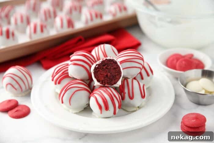 Decadent Red Velvet Bites 9 A charming plate of finished Red Velvet Truffles, with one truffle cut open to perfectly display its rich red cake interior beautifully enrobed in a white chocolate shell with a delicate red drizzle.