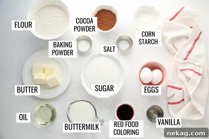 A flat lay photograph showcasing all the essential Red Velvet Cupcakes ingredients: flour, cocoa powder, corn starch, baking powder, salt, butter, sugar, eggs, oil, buttermilk, vibrant red food coloring, and vanilla extract.