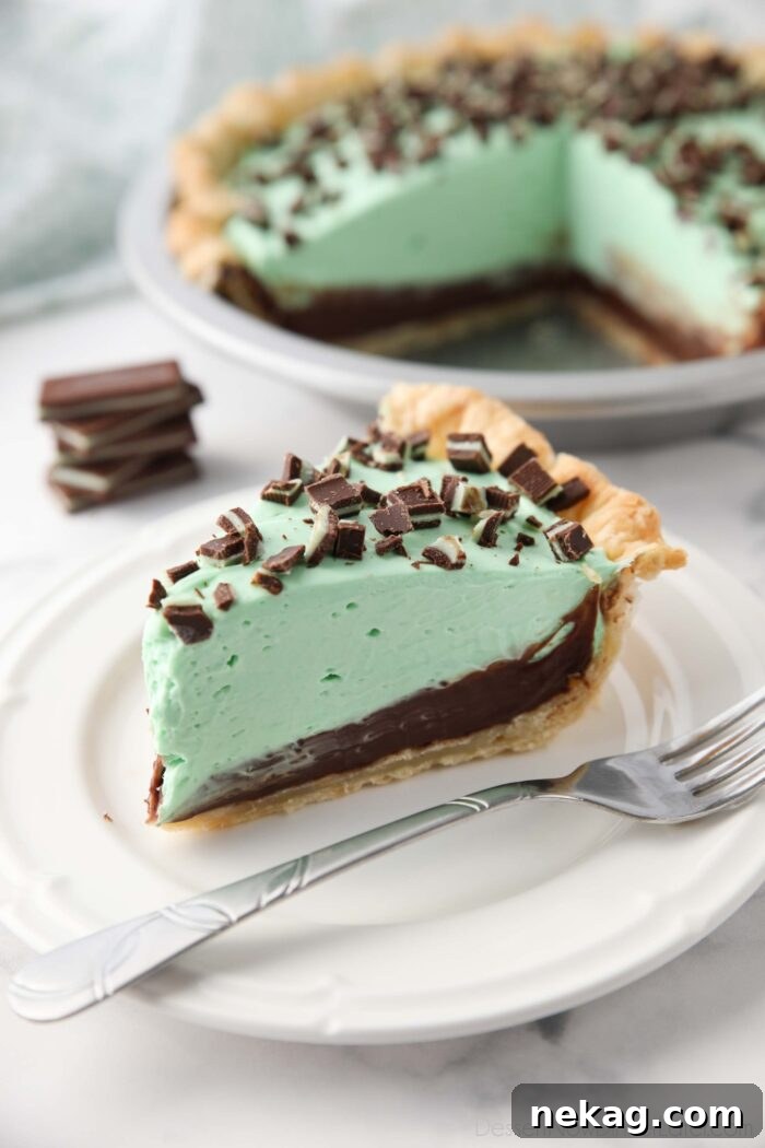 Decadent Chocolate Mint Dream 2 Slice of chocolate mint pie on a plate with layers of pastry crust, chocolate ganache, mint no bake cheesecake, and chopped Andes mints.