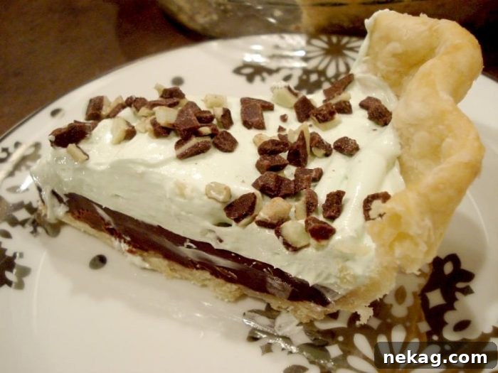 Decadent Chocolate Mint Dream 12 Slice of chocolate mint pie on a plate with layers of pastry crust, chocolate ganache, mint no bake cheesecake, and chopped Andes mints.
