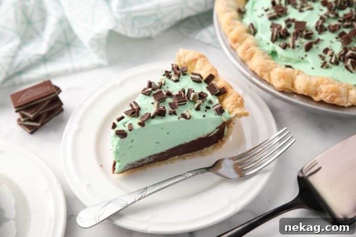 Decadent Chocolate Mint Dream 10 Slice of chocolate mint pie on a plate with layers of pastry crust, chocolate ganache, mint no bake cheesecake, and chopped Andes mints.