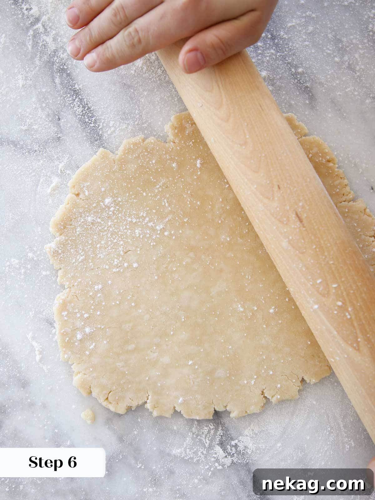 Flaky Crisco Pie Crust Recipe 11 Crisco pie dough being rolled with a wooden rolling pin on a marble surface, creating a smooth, even sheet.