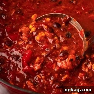 A ladle full of smoky chipotle chili, poised over the pot, ready to be served.