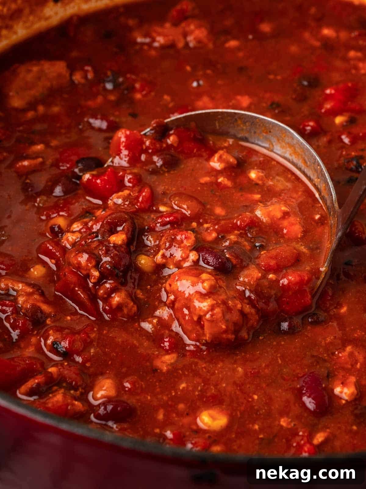 A ladle expertly scooping a generous portion of chipotle chili from a pot, ready for serving.