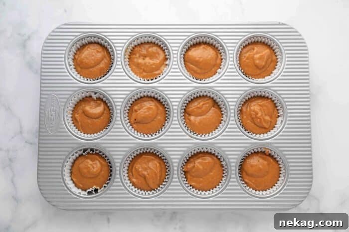Pumpkin cake batter spooned into a muffin pan lined with paper cups, ready for topping.