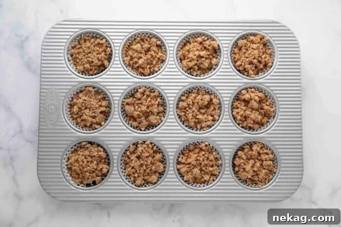 Pumpkin muffin batter in a lined muffin pan, generously topped with crumb streusel before baking.