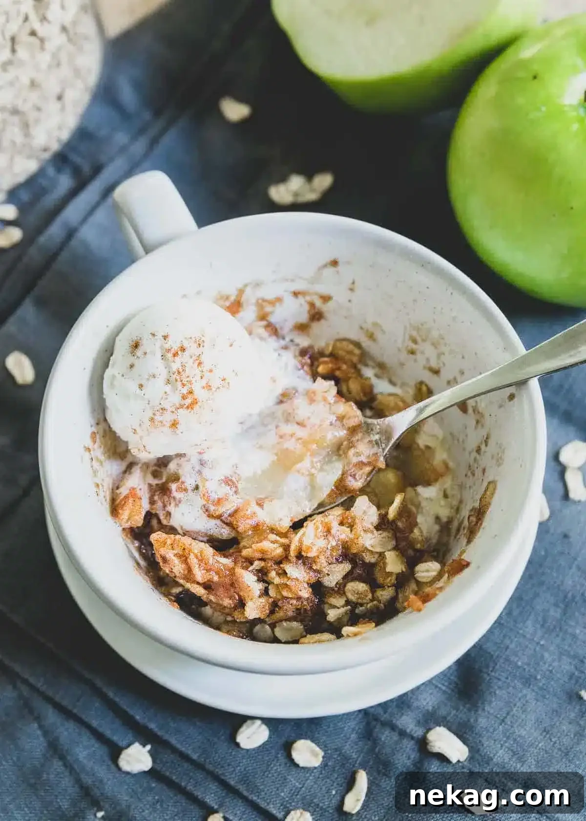 A warm bowl of microwave apple crisp, generously topped with melting vanilla ice cream and a spoon.
