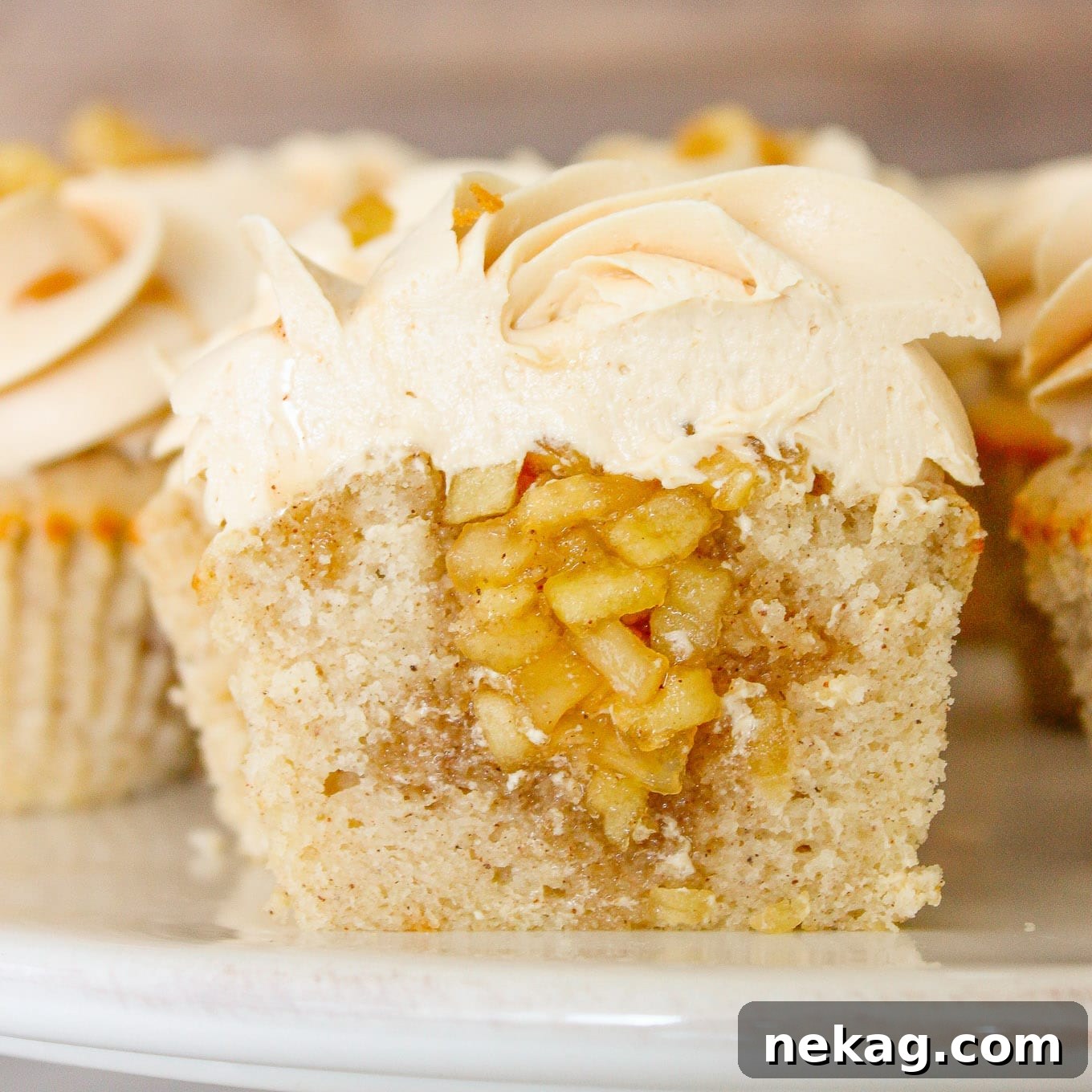 Two caramel apple cupcakes, one sliced open to reveal a spiced apple compote filling, adorned with luscious salted caramel buttercream.