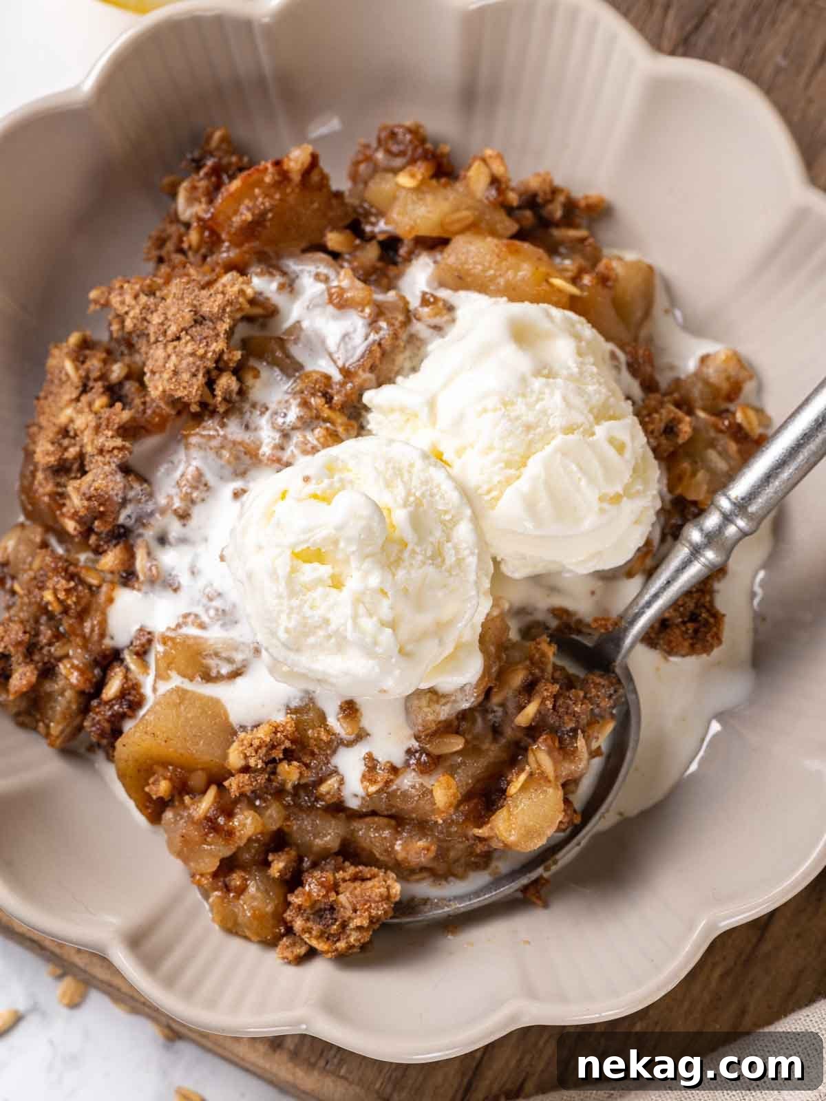 A cozy bowl of apple crisp, topped with a scoop of melting vanilla ice cream and a vintage pewter spoon.